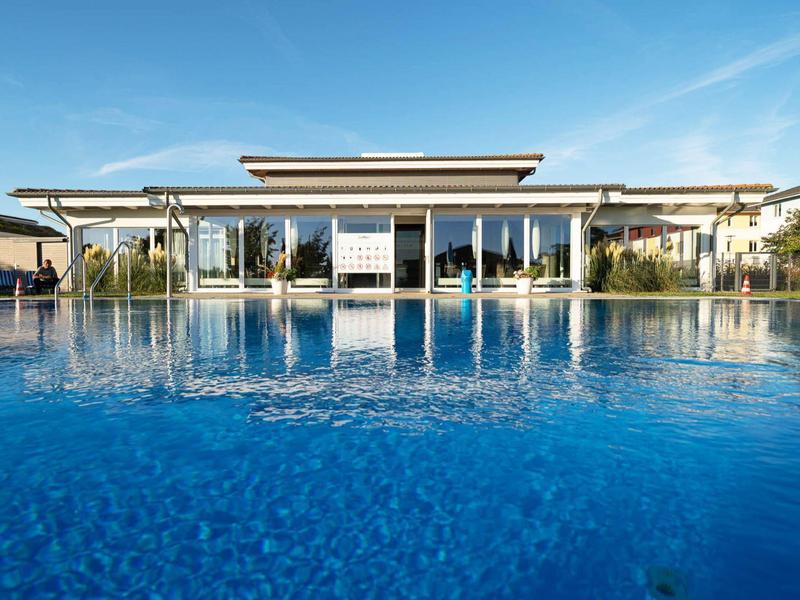 Großer moderner Pool mit klarem blauem Wasser vor Glas-Fassadenhaus unter blauem Himmel.