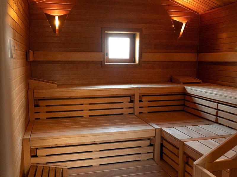 Holzsauna mit mehrstufigen Sitzbänken, warmem Licht und kleiner Fensteröffnung.