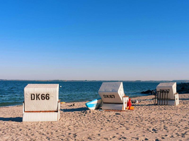 Strand mit drei weißen Strandkörben, blauem Himmel und ruhiger Ostsee im Hintergrund.