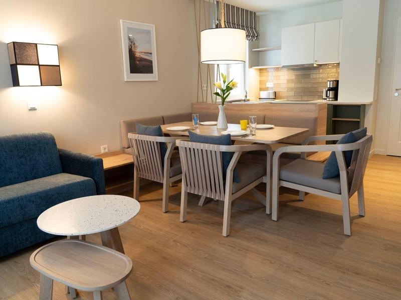 Gemütliches Esszimmer mit Holztisch, vier Stühlen, blauem Sofa und weißem Hocker auf Parkettboden.