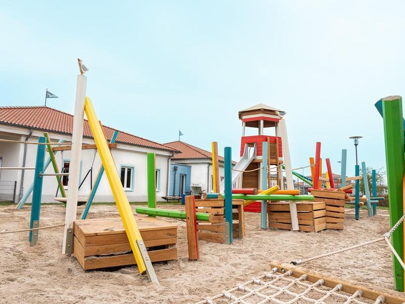 Bunter, moderner Kinderspielplatz mit Holzgerüsten, Kletternetzen und Sandboden bei Tageslicht.