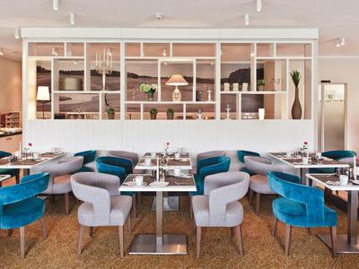 Modernes Restaurant mit blauen und grauen Stühlen, rechteckigen Tischen und offener Regalwand.