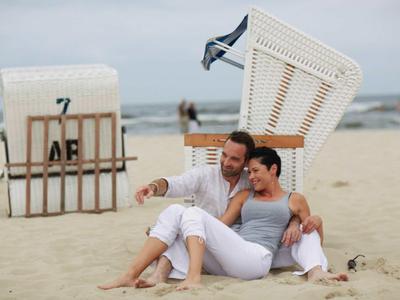 Paar sitzt entspannt am Strand vor einem Strandkorb mit Meer im Hintergrund