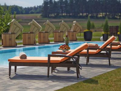 Sonnenliegen mit orangen Polstern neben einem Pool und Strandkörben im Hintergrund.