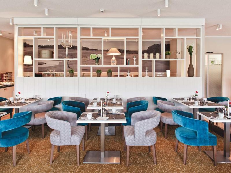 Modernes Restaurant mit blauen und grauen Stühlen, rechteckigen Tischen und offener Regalwand.