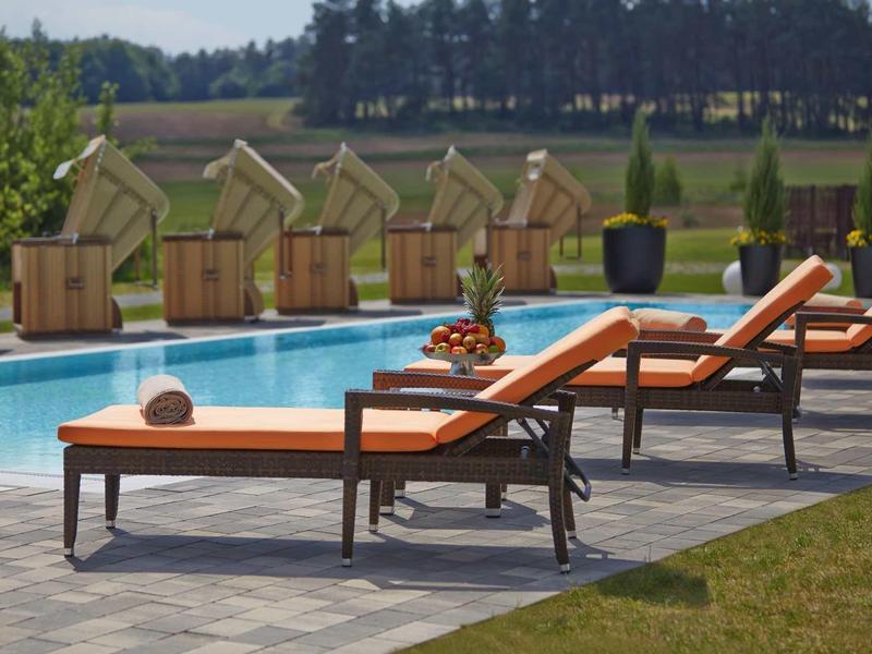 Mehrere orange Liegestühle stehen neben einem blauen Pool mit grüner Landschaft im Hintergrund.