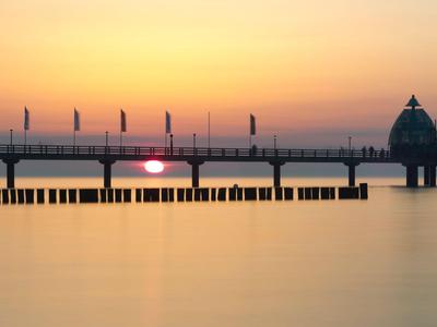Sonnenuntergang über einer langen Seebrücke mit ruhigem Wasser und einem runden Pavillon.