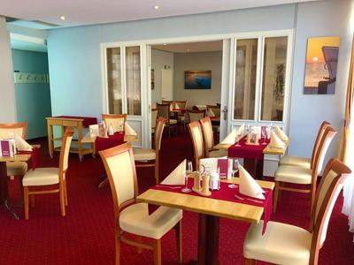 Eleganter Speisesaal mit rotem Teppich, Holztischen und cremefarbenen Stühlen in einem Hotel.