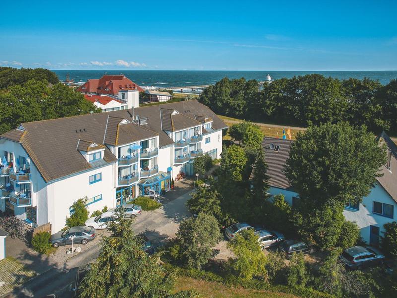 Ein Hotelgebäude mit mehreren Stockwerken und Balustraden, umgeben von Bäumen und Blick auf das Meer.