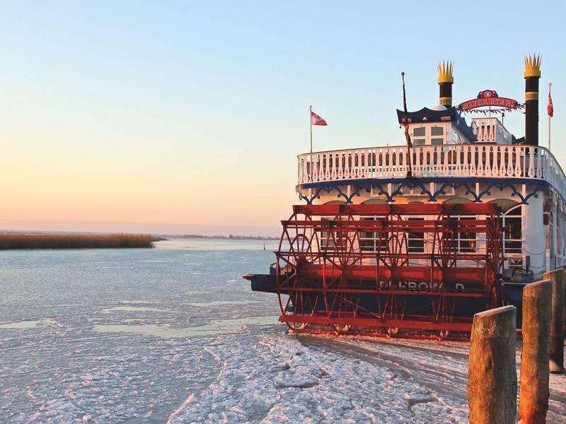 Raddampfer am gefrorenen Fluss bei Sonnenuntergang neben einem Steg.
