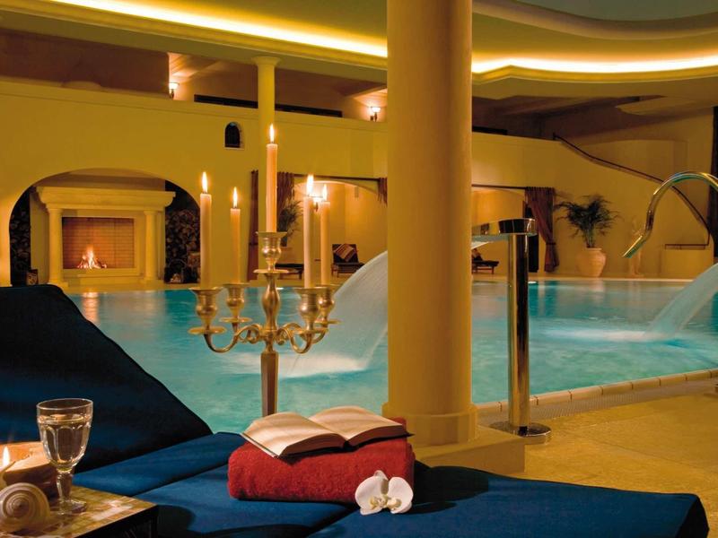 Innenpool mit blauen Liegen, Kerzenleuchter, Handtüchern und warmem gelbem Licht.