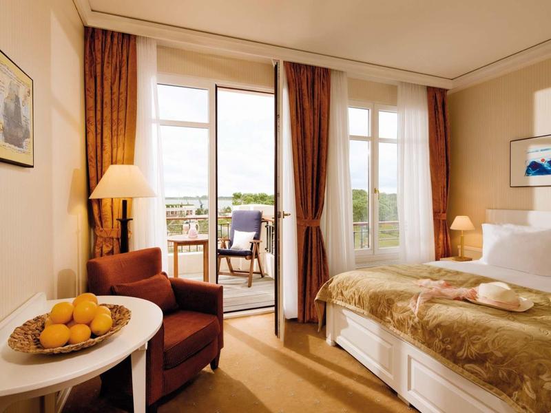 Helles Schlafzimmer mit Bett, Sessel, Tisch, Früchten und Balkon mit Aussicht.