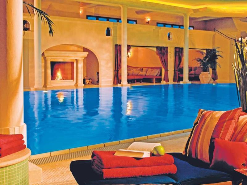 Innenpool mit blauem Wasser, umgeben von Säulen, gemütlichen Sitzmöbeln und warmem Licht.