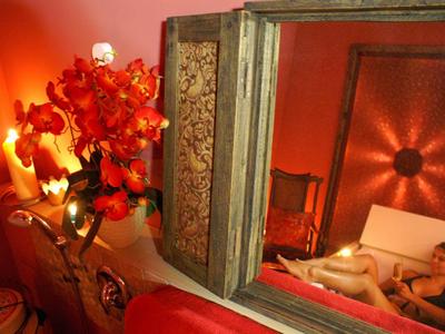 Romantisch ingericht kamer met kaarsen, rode bloemen en spiegel naast een bed.