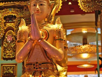 Gouden beeld met gevouwen handen voor een sierlijke tempelachtergrond.