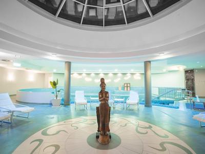 Eleganter Innenpoolbereich mit Liegestühlen und dekorativer Statue unter einer Glaskuppel