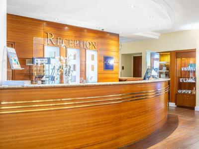 Lichte hotel lobby met een glanzend gebogen houten receptiebalie en receptiebord.