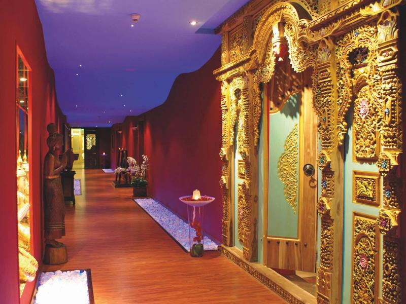 Gang met houten vloer en rijk versierde gouden deuren in een hotel.