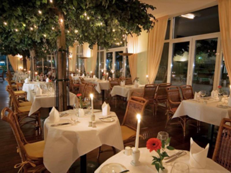 Elegant restaurant met witte tafelkleden, kaarslicht en een boom in het midden.