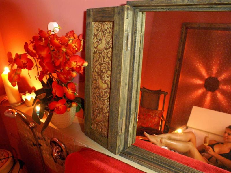 Romantisch ingericht kamer met kaarsen, rode bloemen en spiegel naast een bed.