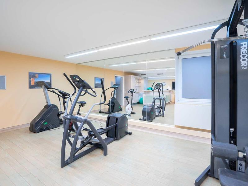 Moderne fitnessruimte met crosstrainer, loopband en krachtapparaat voor grote spiegel.