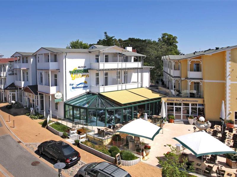 Mehrere Gebäude in Küstennähe mit Terrasse, Sonnenschirmen und parkenden Autos an der Straße.