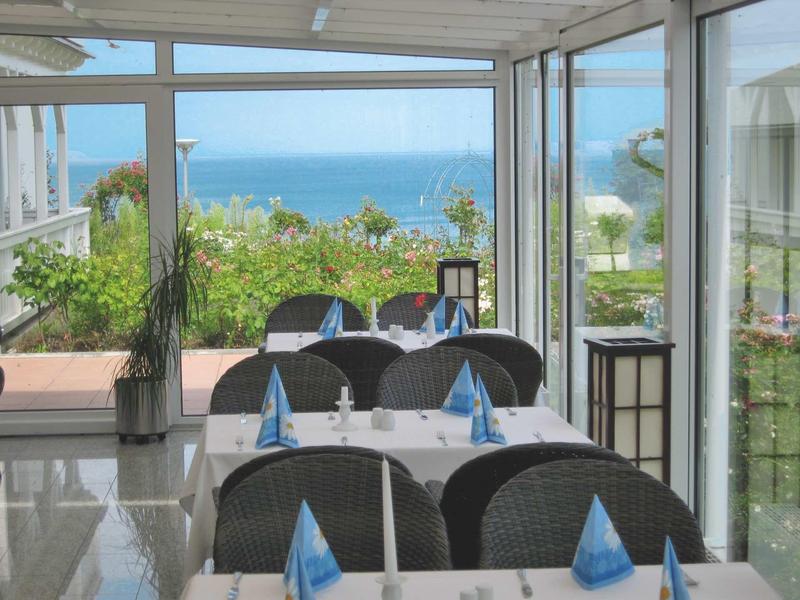 Helles Restaurant mit großen Fenstern, Meerblick, Tischen mit weißen Tüchern und blau gefalteten Servietten.