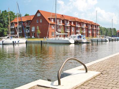 Segelboote sind am Steg eines ruhigen Gewässers vor einem Hotel mit rotem Dach vertäut.