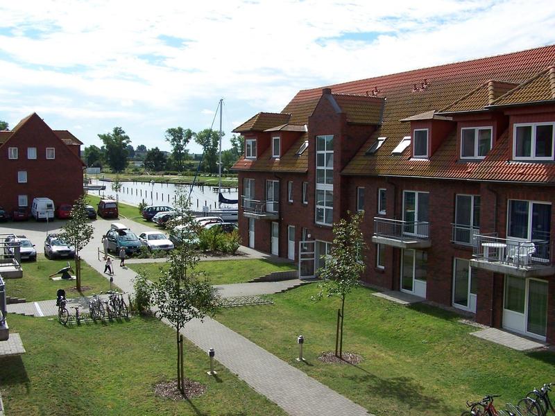 Moderner Hotelkomplex mit roten Dächern neben einem See und Parkplatz.