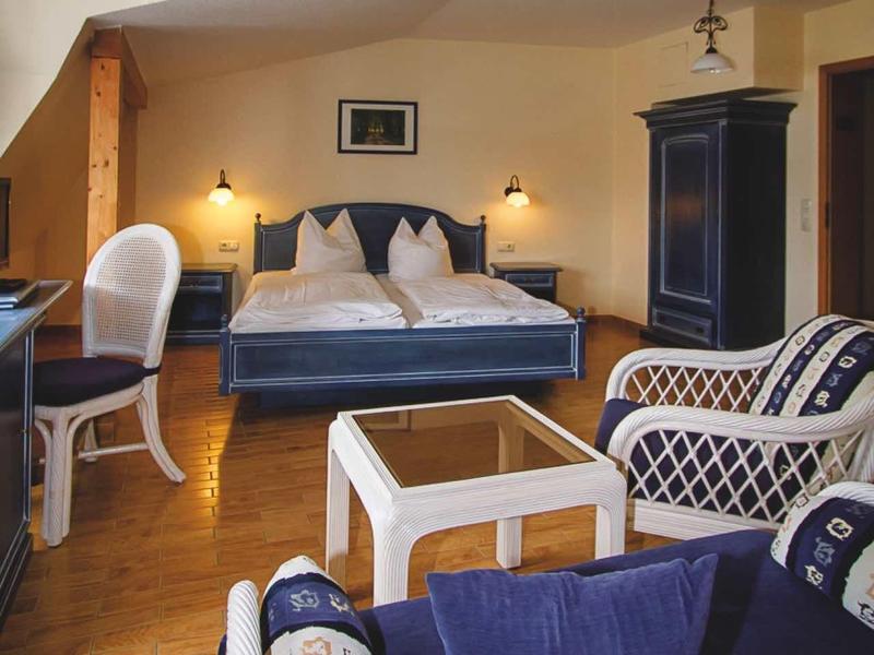 Gemütliches Wohnzimmer mit blauen Sesseln, Holzboden und einem großen Bett im Hintergrund.