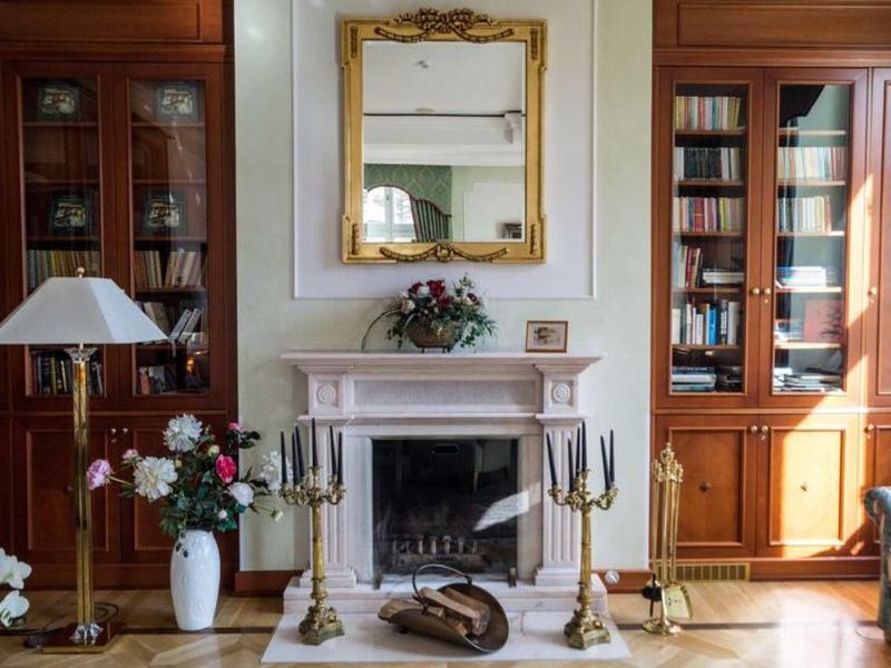 Elegantes Wohnzimmer mit Kaminsims, Goldspiegel und Holzmöbeln, dekoriert mit Blumen und Kerzen.