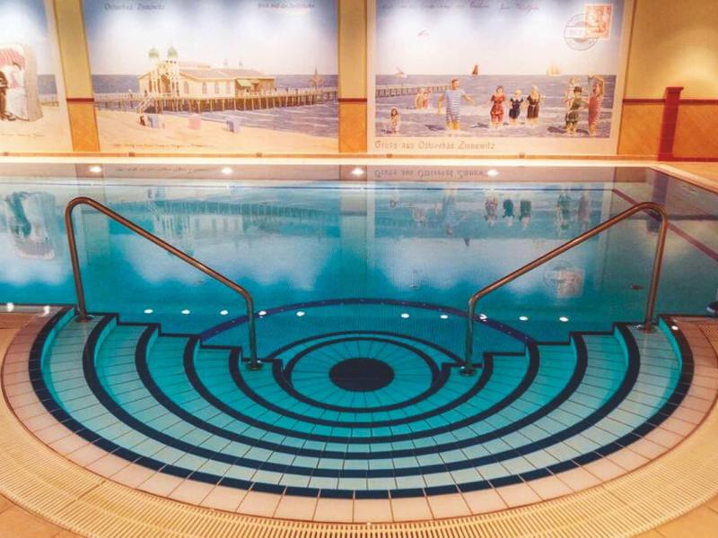 Innenbecken mit kreisförmigen Fliesenmustern und Handläufen, helle Wandbilder im Hintergrund.