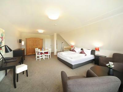 Großes Zimmer mit Doppelbett, Sofas, Schreibtisch, Kleiderschrank und Esstisch in hellen Farben.