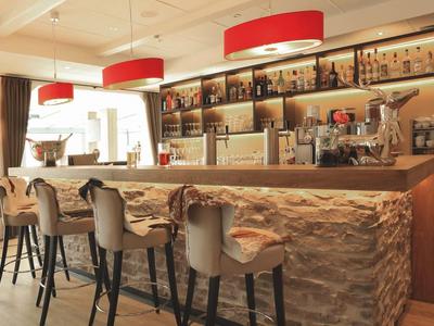 Moderne Bar mit hellem Holz, roter Beleuchtung, bequemen Stühlen und gut bestücktem Regal.