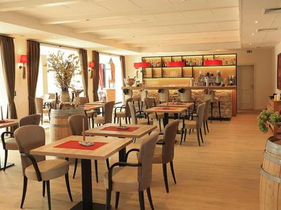 Moderner Gastraum mit Holztischen, beigen Stühlen, großen Fenstern und warmem Licht.