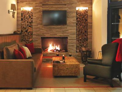 Gemütlicher Wohnzimmerbereich mit Kamin, Sofa, Sessel und Holzstapel an den Wänden.