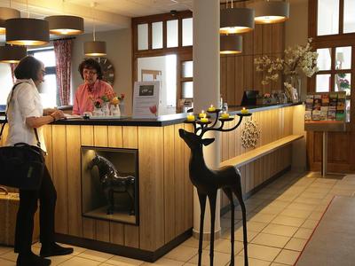 Hotelrezeption mit holzverkleidetem Tresen, dekorativem Rentier und zwei Personen im Gespräch.