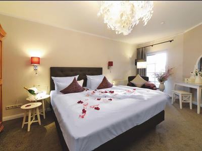 Helles Schlafzimmer mit Doppelbett, weißen Bettwäsche mit Rosenblättern und elegantem Kronleuchter.