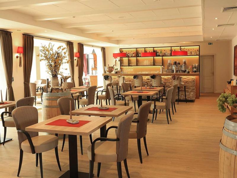 Moderner Gastraum mit Holztischen, beigen Stühlen, großen Fenstern und warmem Licht.