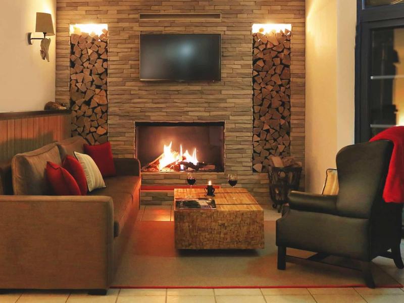 Gemütliches Wohnzimmer mit Kamin, braunem Sofa, schwarzem Sessel und Flachbildfernseher an Wand.