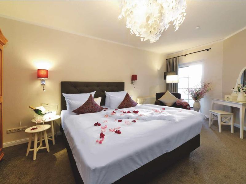 Gemütliches Schlafzimmer mit Doppelbett, Holzmöbeln, Rosenblättern und weicher Beleuchtung.