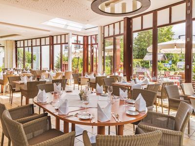 Helles Restaurant mit rund angeordneten Tischen, Stühlen und Außenterrasse bei Sonnenschein.