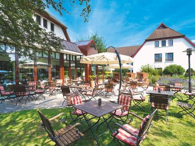 Terrasse mit Stühlen und Tischen vor einem Hotelgebäude bei sonnigem Wetter.