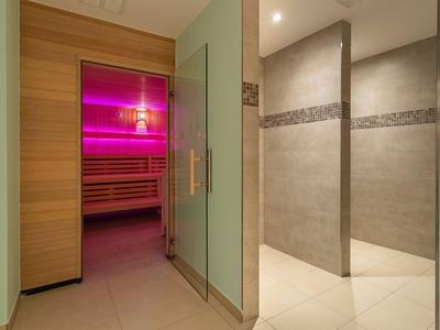 Moderner Wellnessbereich mit Sauna und großzügigem Duschbereich mit beigen Fliesen.