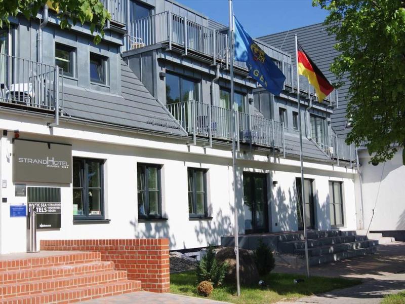 Modern three-story building with white walls, many windows, and three flags