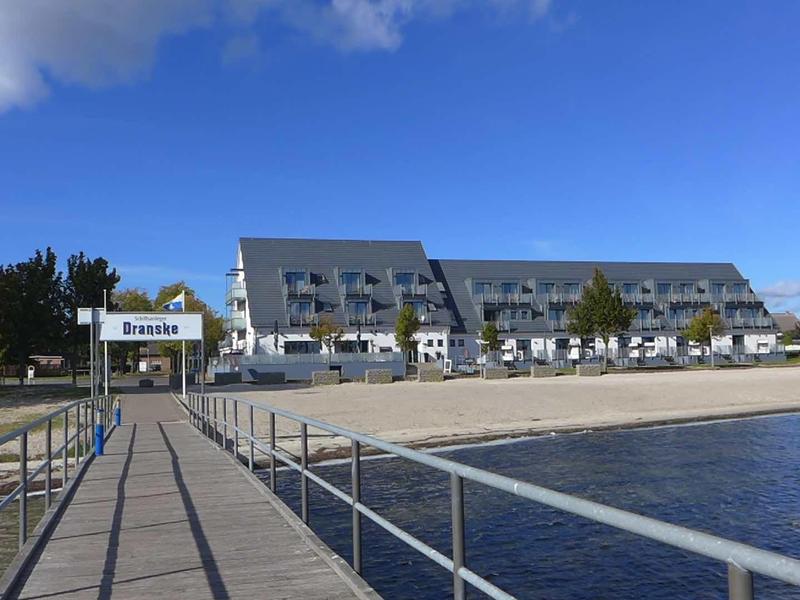 Modern hotel with brick facade and large parking lot by the lakeshore under clear sky.