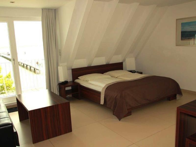 Bright bedroom with double bed, wooden furniture, and balcony access overlooking greenery.