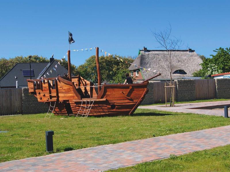 A wooden pirate ship playground structure on a grassy area with a paved walkway.