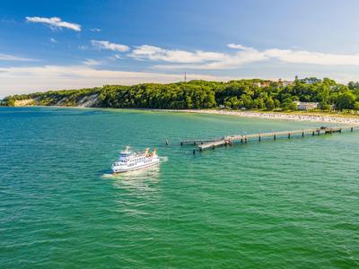 Boat sailing on green water near a wooded coastline with a long pier.