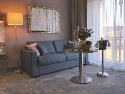 Modernes Wohnzimmer mit grauem Sofa, Stehlampe, rundem Tisch und großen Fenstern mit Vorhängen.